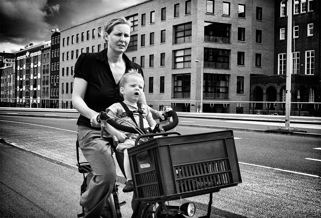A woman carrying a child on a bicycle along a street.
